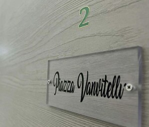 Eine Holzwand mit einer Metallplatte, auf der „Piazza Vanvitelli“ steht.