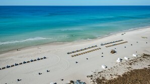 Una playa con hileras de sillas azules y sombrillas, arena y el océano.
