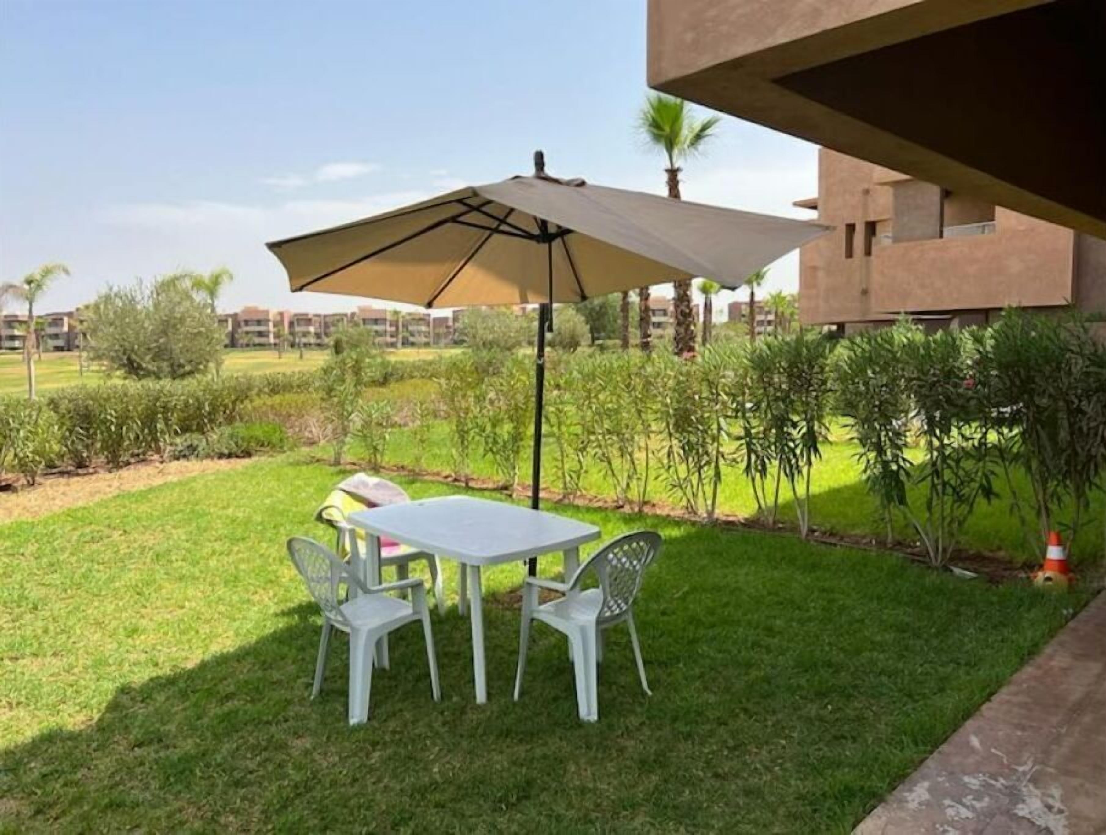 A patio with a table and chairs, an umbrella, and a view of a residential area with buildings and greenery.