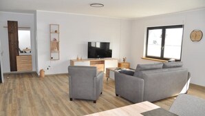 Un salon moderne avec un canapé gris, un téléviseur et une table à manger en bois.