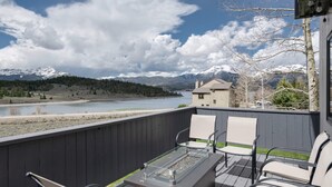 Een balkon met een tafel en stoelen met een glazen blad, met uitzicht op een rivier en bergen.