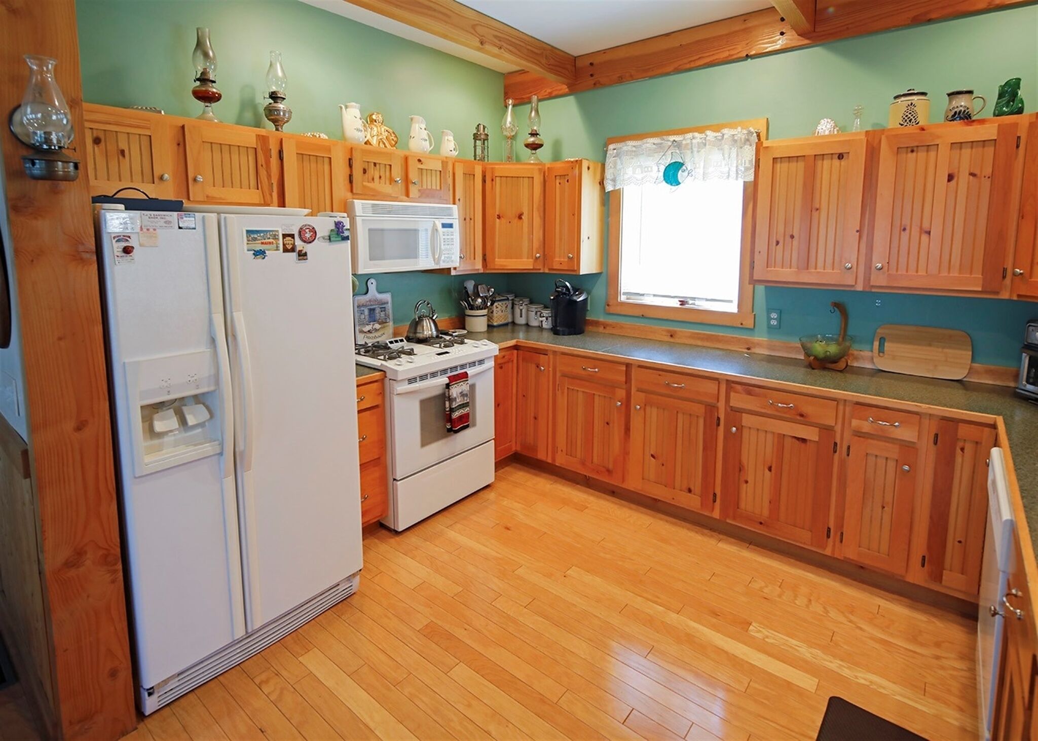 Une cuisine avec des meubles de rangement en bois, un réfrigérateur, un four à micro-ondes, une cuisinière et une fenêtre avec des rideaux.