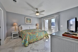 Une chambre à coucher comprenant un lit, deux lampes de chevet, un ventilateur de plafond, une télévision et un balcon avec des rideaux.