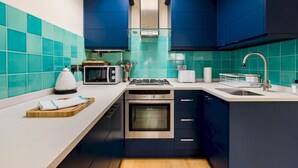 Une cuisine moderne avec des carreaux de couleur turquoise, des meubles de rangement bleu foncé, une cuisinière à gaz, un four à micro-ondes et un four encastré.
