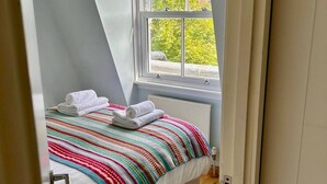 Une chambre avec un plafond en pente, une fenêtre agrémentée d’une lambrequin rouge, un lit recouvert d’une couverture rayée aux couleurs vives et des serviettes blanches.