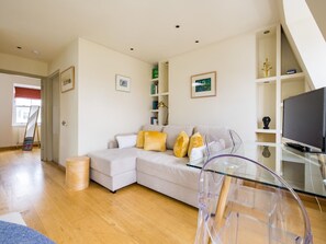 Uma sala de estar moderna com um sofá de cor clara, uma mesa de centro de vidro e uma televisão de tela plana.