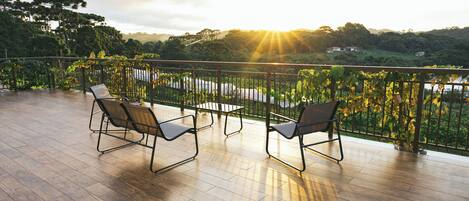 A wooden deck with two chairs and a table, overlooking a lush landscape with trees and a body of water.