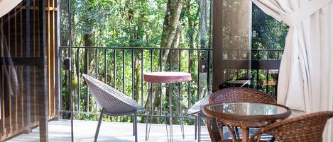 A balcony with wicker chairs and a small table, overlooking a lush garden.