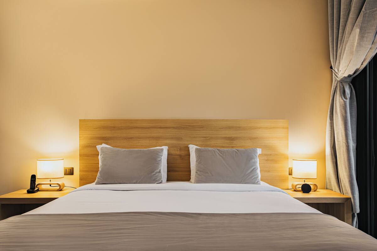 Ein Hotelzimmer mit hölzernem Kopfteil, zwei Nachttischlampen, einem Telefon und einem Bett mit weißer Bettwäsche.