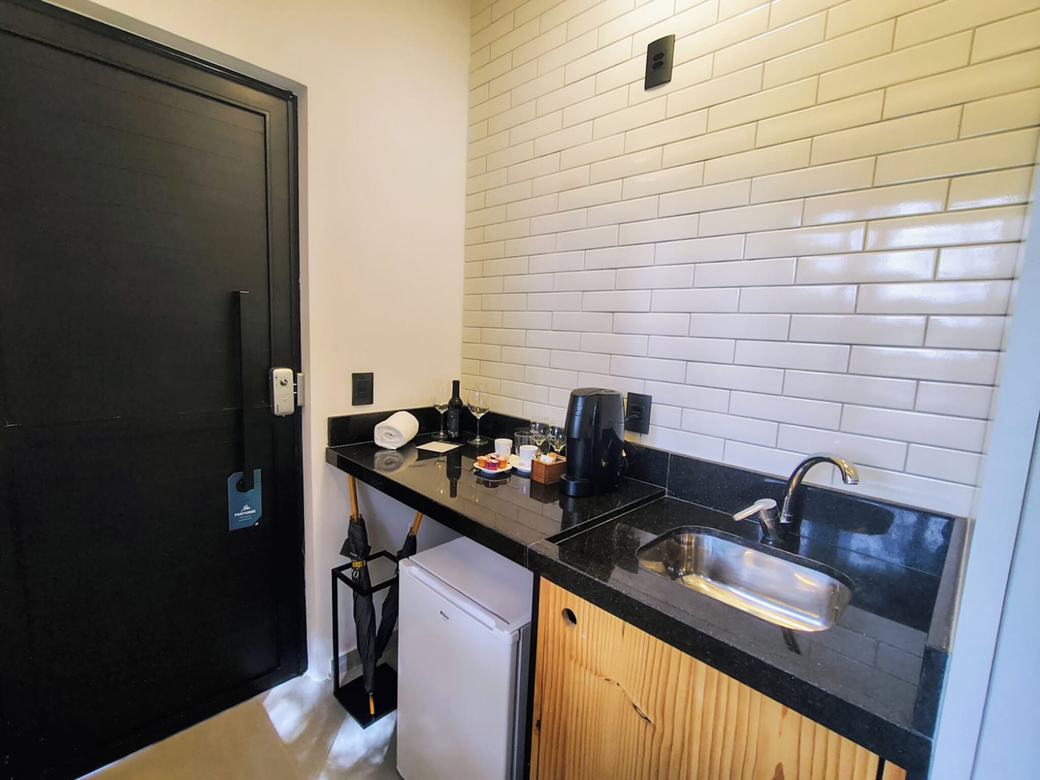 Una cocina compacta con encimera negra, salpicadero de azulejos blancos y un lavabo integrado.