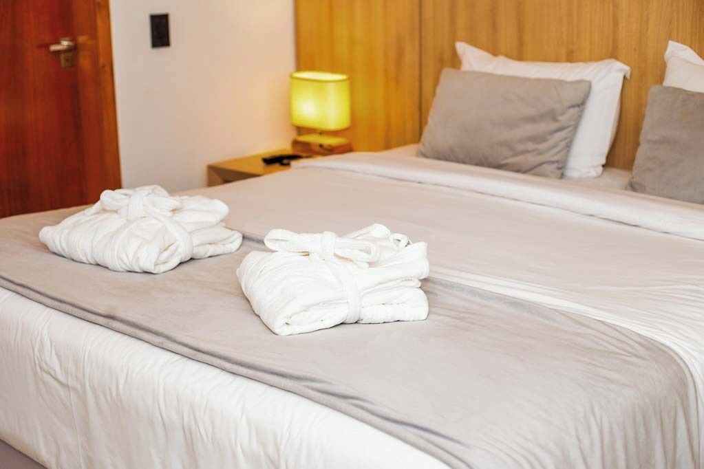 Una cama bien tendida con sábanas blancas y dos toallas dobladas sobre ella.