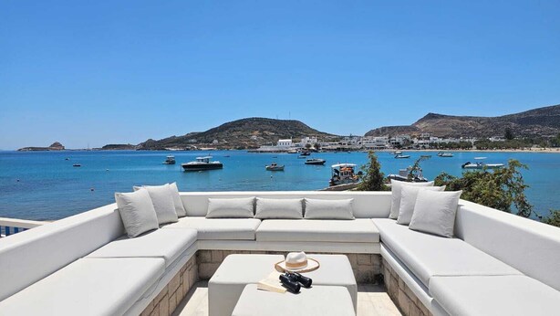 Un área de estar exterior blanca con vista a un puerto y barcos.