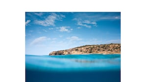 Un paisaje costero con aguas azul cristalino y una colina rocosa al fondo.