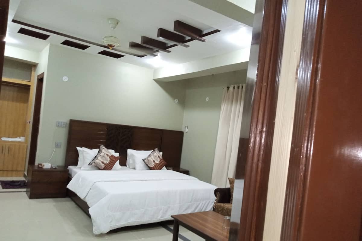 Habitación de hotel con cama, mesitas de noche, cabecera de madera, ventilador de techo y ventana con cortinas.