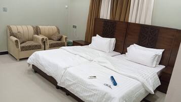 A hotel room with a bed, two chairs, a nightstand, and a curtain.