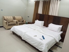 A hotel room with a bed, two chairs, a nightstand, and a curtain.