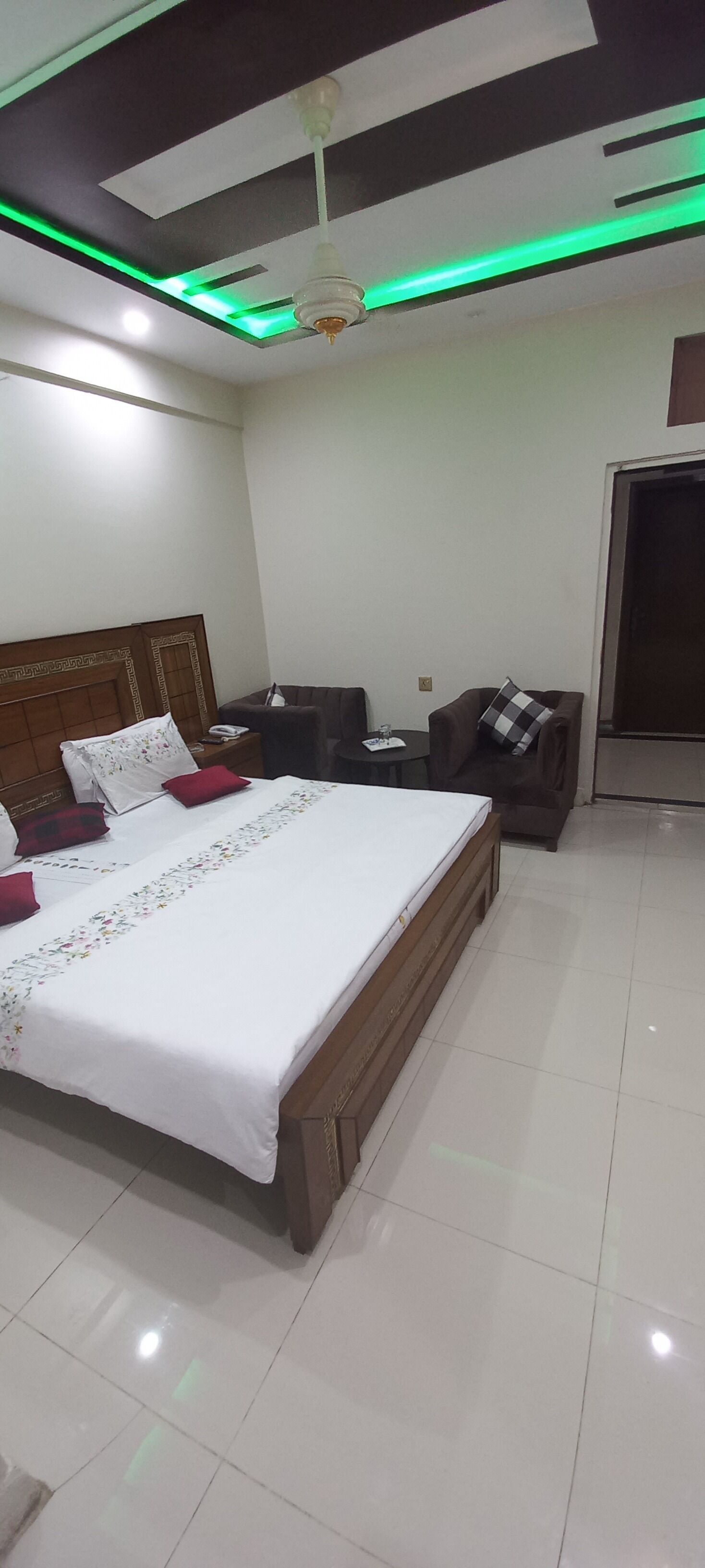 Habitación de hotel con una cama grande, cabecera de madera, una mesita, un sofá y un ventilador de techo.