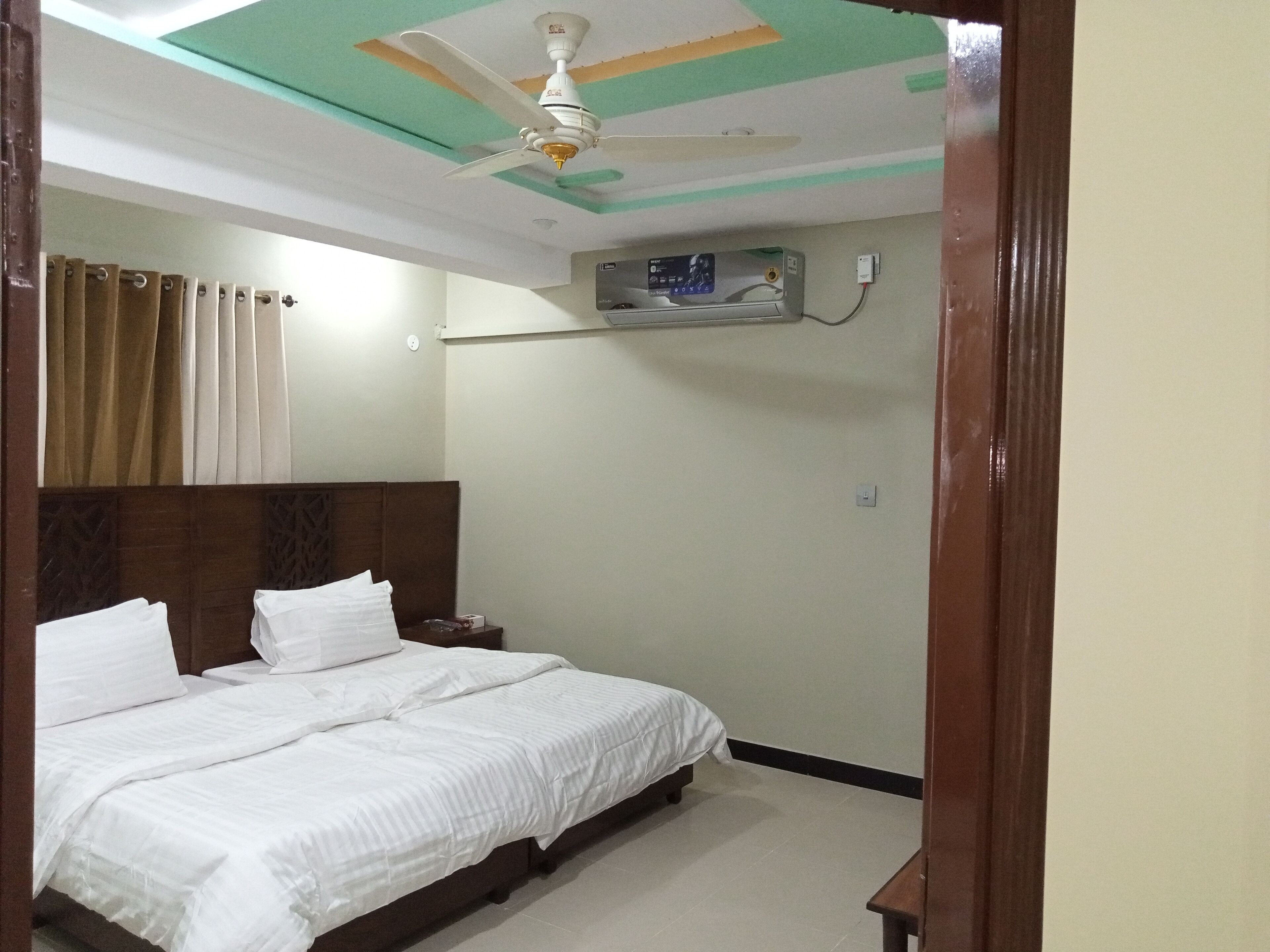 Une chambre d’hôtel avec un lit, un ventilateur de plafond, un climatiseur fixé au mur et des rideaux.