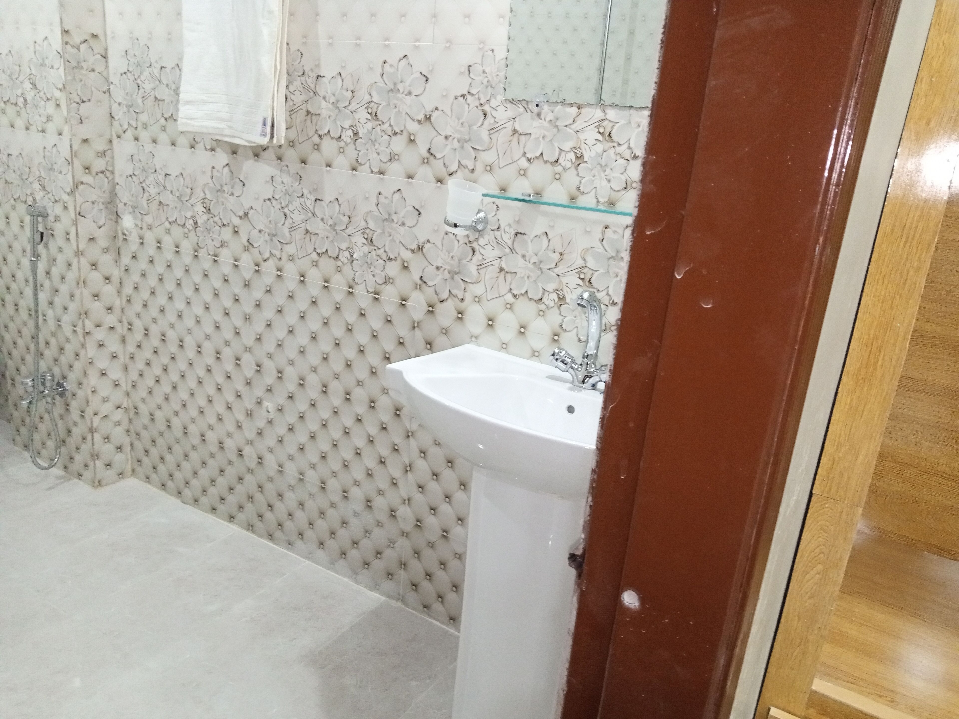 A bathroom with a white sink, a glass shelf, and a shower area.