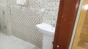 A bathroom with a white sink, a glass shelf, and a shower area.
