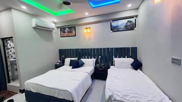 A modern hotel room with two beds, a large window with a mountain view, and a unique ceiling design with green and blue lighting.