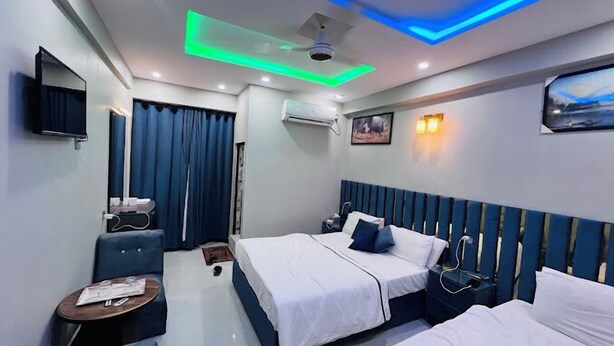 A hotel room with two beds, a TV, an air conditioner, and a painting on the wall. - Hotel Almarkaz (Islamabad)
