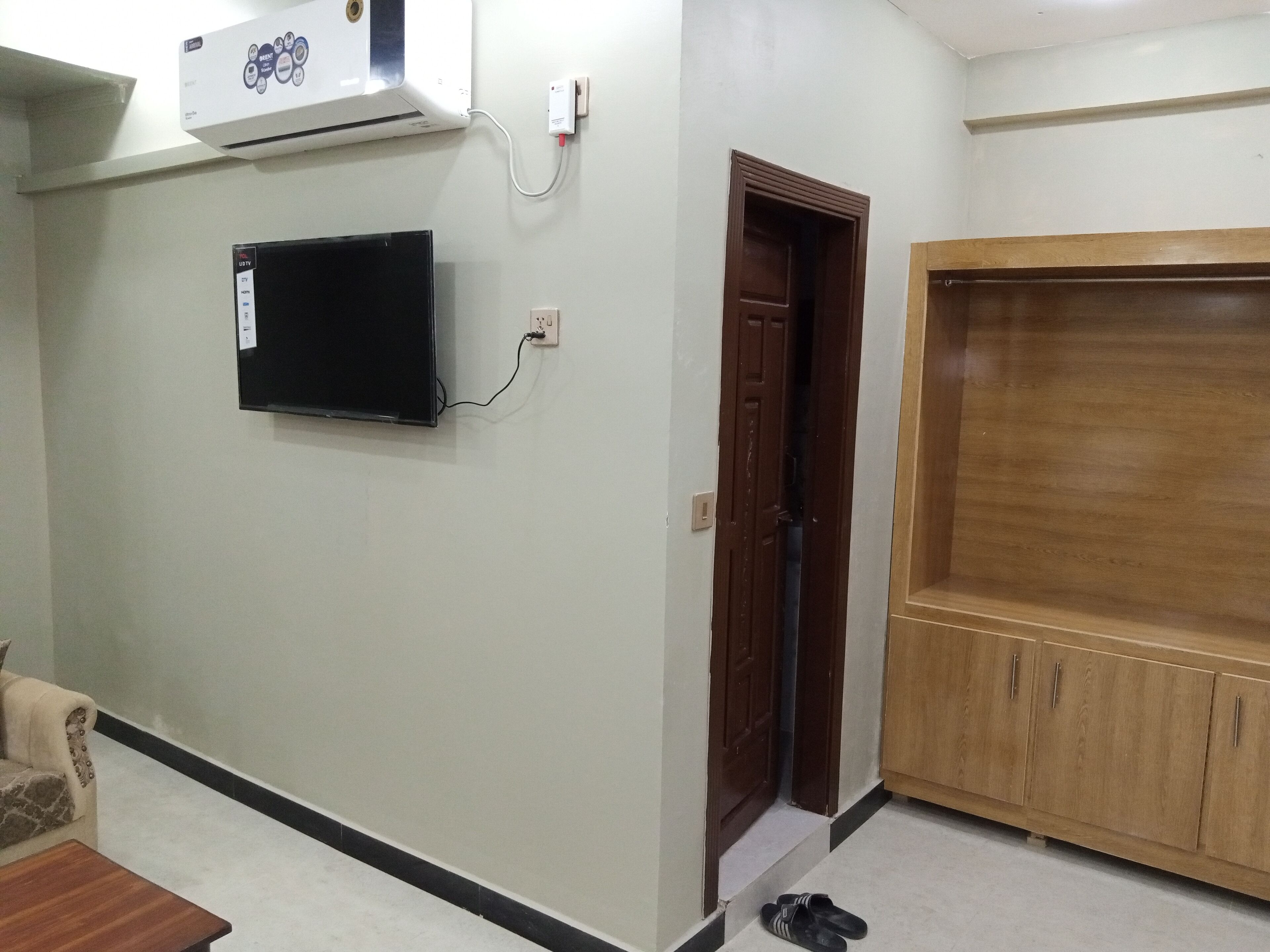 Una habitación con aire acondicionado instalado, televisor de pared, armario de madera y una puerta que da a otra habitación.