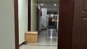 A hallway with a wooden door frame, a tiled floor, and a light fixture on the ceiling. - Hotel Almarkaz (Islamabad)