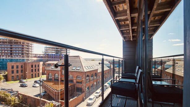 A balcony with a view of a cityscape, including a brick building and a modern structure.
