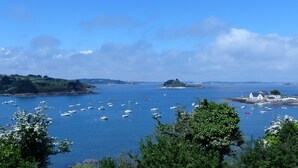 Vista costera con barcos en el agua, una pequeña isla y un edificio de fachada blanca.