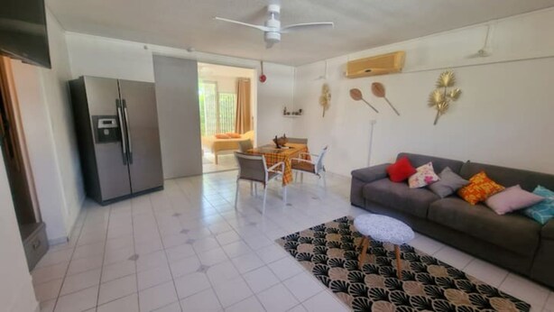 Uma sala de estar com um sofá cinza, um tapete estampado e um espaço de jantar com mesa e cadeiras.