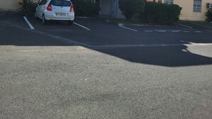 Um edifício de vários andares com escadaria central, aparelhos de ar condicionado e um carro estacionado.
