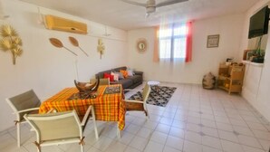 Uma sala de jantar com mesa posta para quatro pessoas, um sofá e uma televisão no canto.
