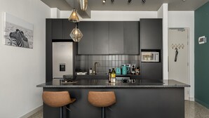 A modern kitchen with dark cabinetry, a central island with stools, a microwave, and a kettle. - Modern Living In Heart of CBD Wifi Pool (Cape Town)