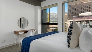 A modern hotel room with a large bed, a desk, and a large window offering a city view. - Modern Living In Heart of CBD Wifi Pool (Cape Town)