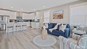 Eine moderne Küche mit weißen Schränken, ein Essbereich mit weißen Stühlen und ein blaues Sofa in einem Wohnzimmer mit einem runden Teppich.