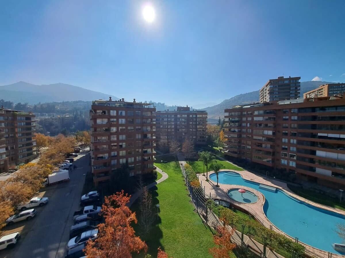 A residential area with apartment buildings, a swimming pool, and a road with parked cars.