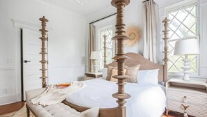 A four-poster bed with a wooden headboard, a bedside table with a lamp, and a window with curtains. - Solar Flair (Atlanta)
