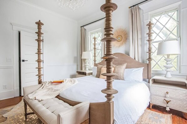 A four-poster bed with a wooden headboard, a bedside table with a lamp, and a window with curtains.