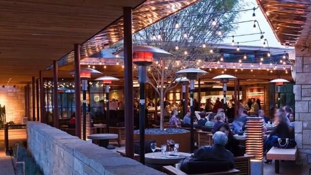 An outdoor dining area with tables and chairs, covered by a roof with string lights. - Solar Flair (Atlanta)