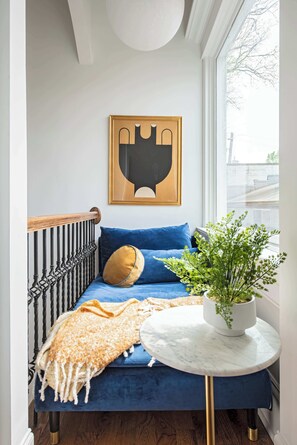 Een hoekappartement met een blauwe bank, een gouden kussen, een witte potplant en een lijstwerk aan de muur.