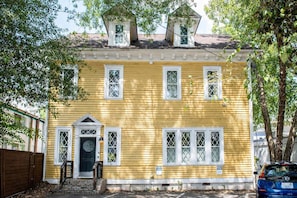 A yellow house with a front door, windows, and a small tower-like structure on the roof.