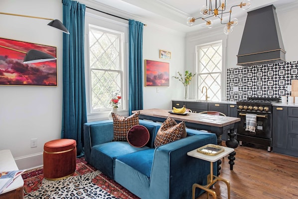 A cozy living room with a blue sofa, a wooden stool, and a patterned rug.