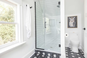 A bathroom with a shower, toilet, and a window with a view of trees.