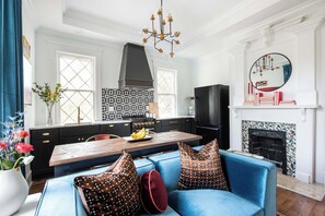 A modern kitchen with a central island, a dining area with a blue sofa, and a fireplace with a mirror above it.
