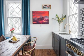 Una cocina con encimera de mármol, estufa y lavamanos. Se observa una mesa de comedor con sillas y un florero con flores.