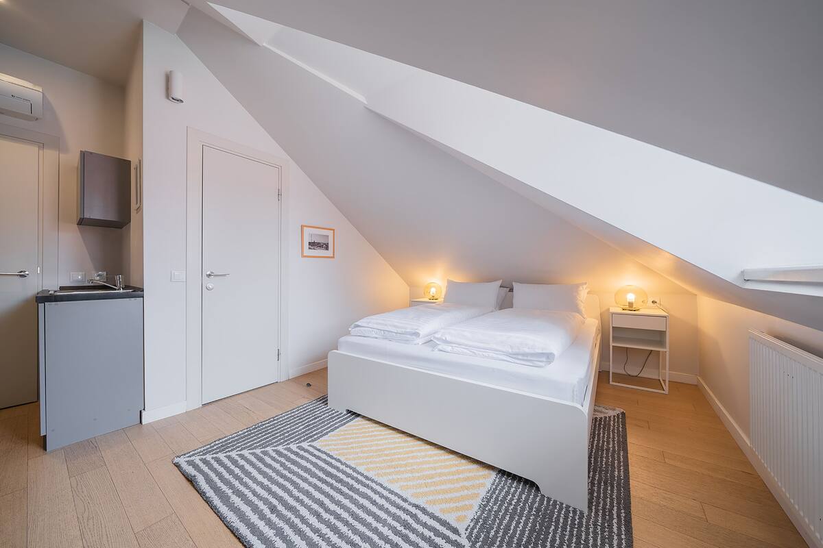 A bedroom with a bed, bedside tables, a desk, and a radiator.