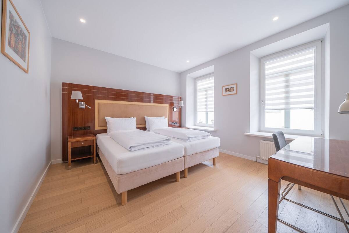 A hotel room with a double bed, bedside tables, a desk, and a window with blinds.