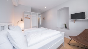 A modern bedroom with a bed, bedside lamp, TV, and a chair. - Lollo Self Check-in Residence - Lollo Luxury (Vilnius)