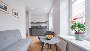 A modern living room with a grey sofa, a round table with a fruit bowl, and a potted plant by a window. - Lollo Self Check-in Residence - Lollo Luxury (Vilnius)